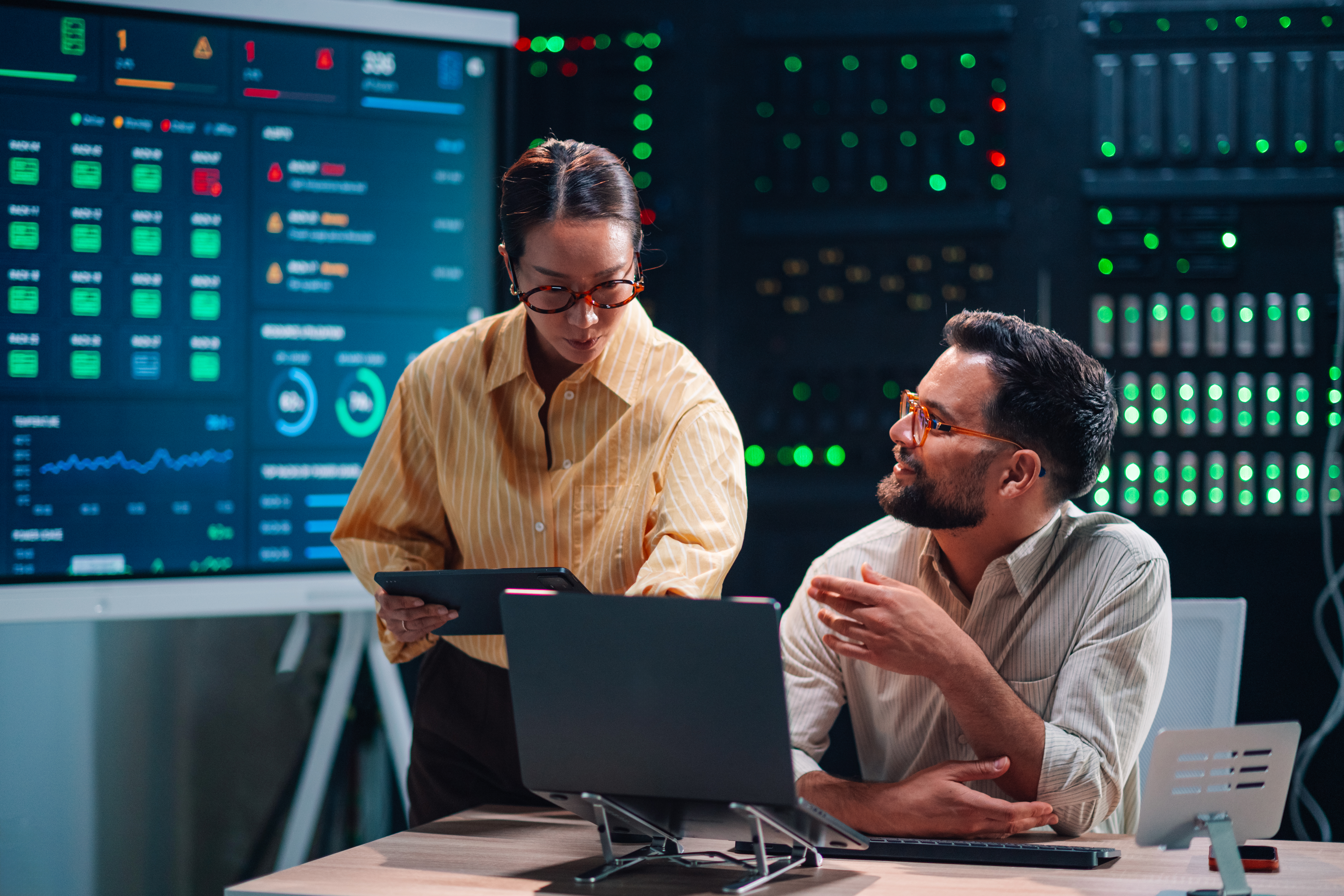 It specialists working in a modern server room, monitoring network status and data flow on a large digital screen